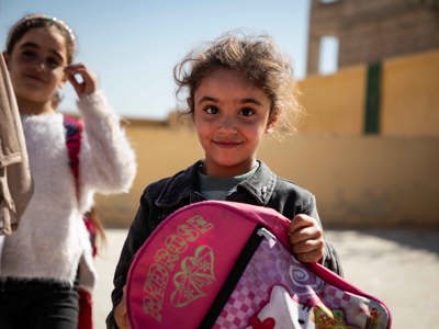 Syrian girl holding a backpack and smiling